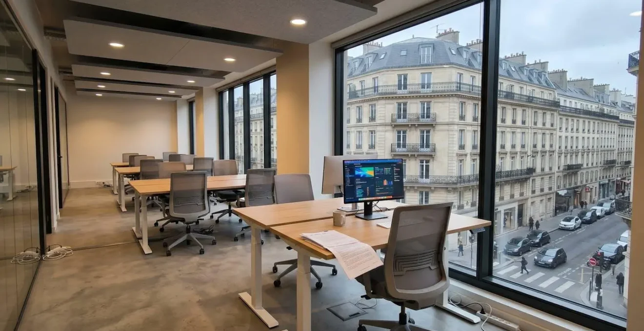 Espace de travail professionnel avec bureau réglable en hauteur, fauteuil ergonomique à support lombaire et large baie vitrée diffusant lumière naturelle